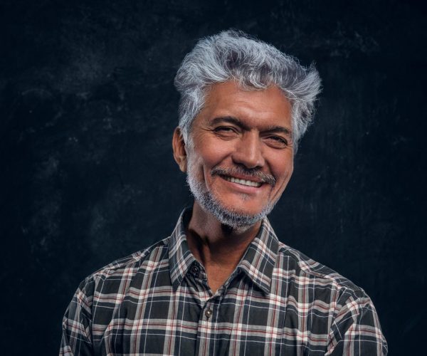 Studio shot of joyful hindu grandfather dressed in plaid shirt against dark background.